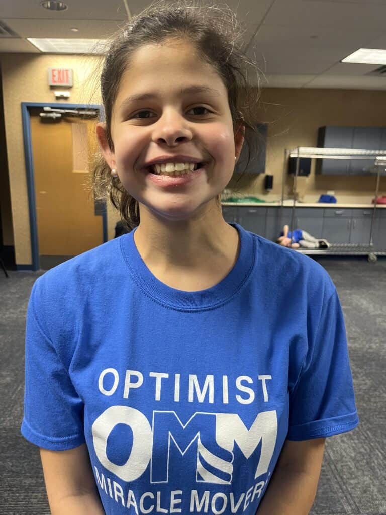 Smiling girl in blue Optimist Miracle Movers T-shirt at martial arts class.