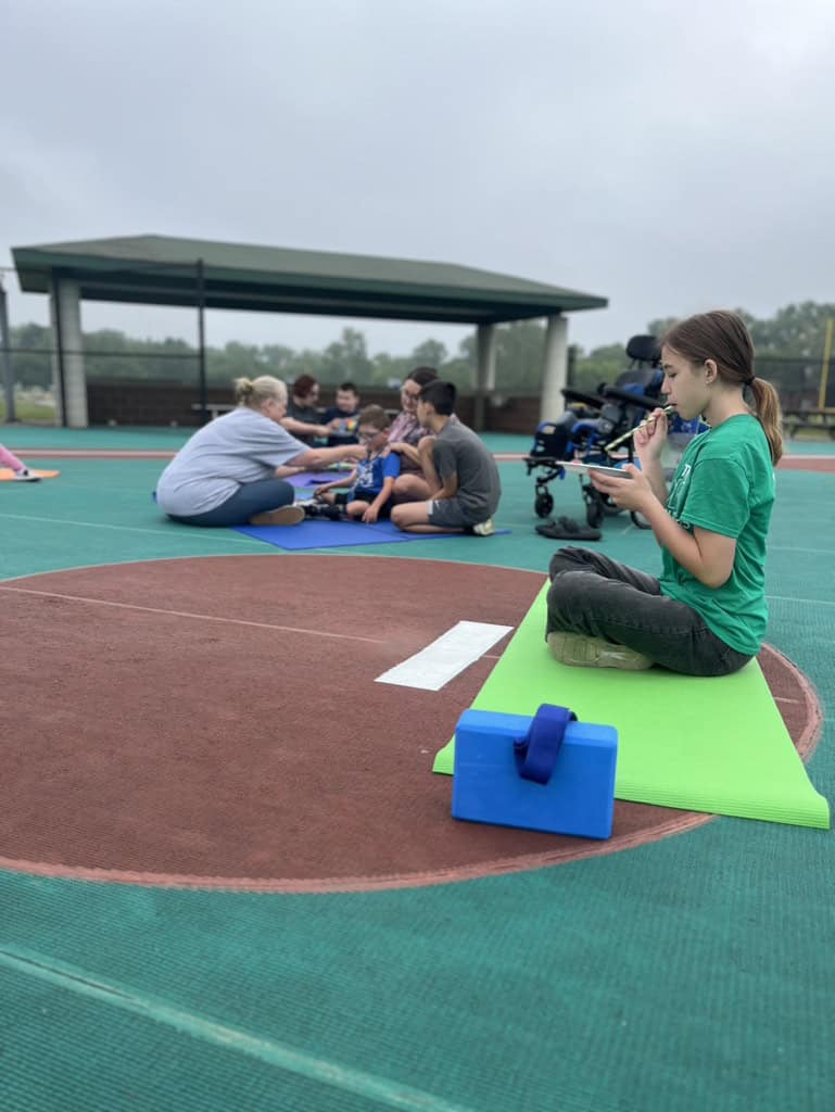 Young girl filming a yoga class outdoors on a sports court.