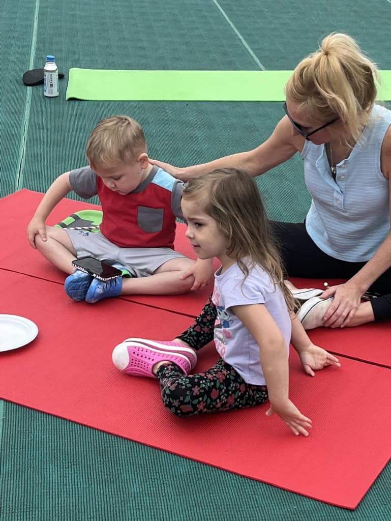 Woman and children practicing stretching on yoga mats outdoors.
